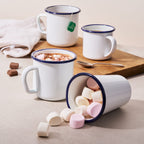 Stack of white enamel mugs with blue rims and handles, candies inside one mug