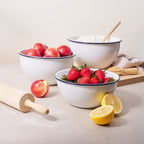 White enamel mixing bowl with blue rim, holding strawberries and wooden utensils